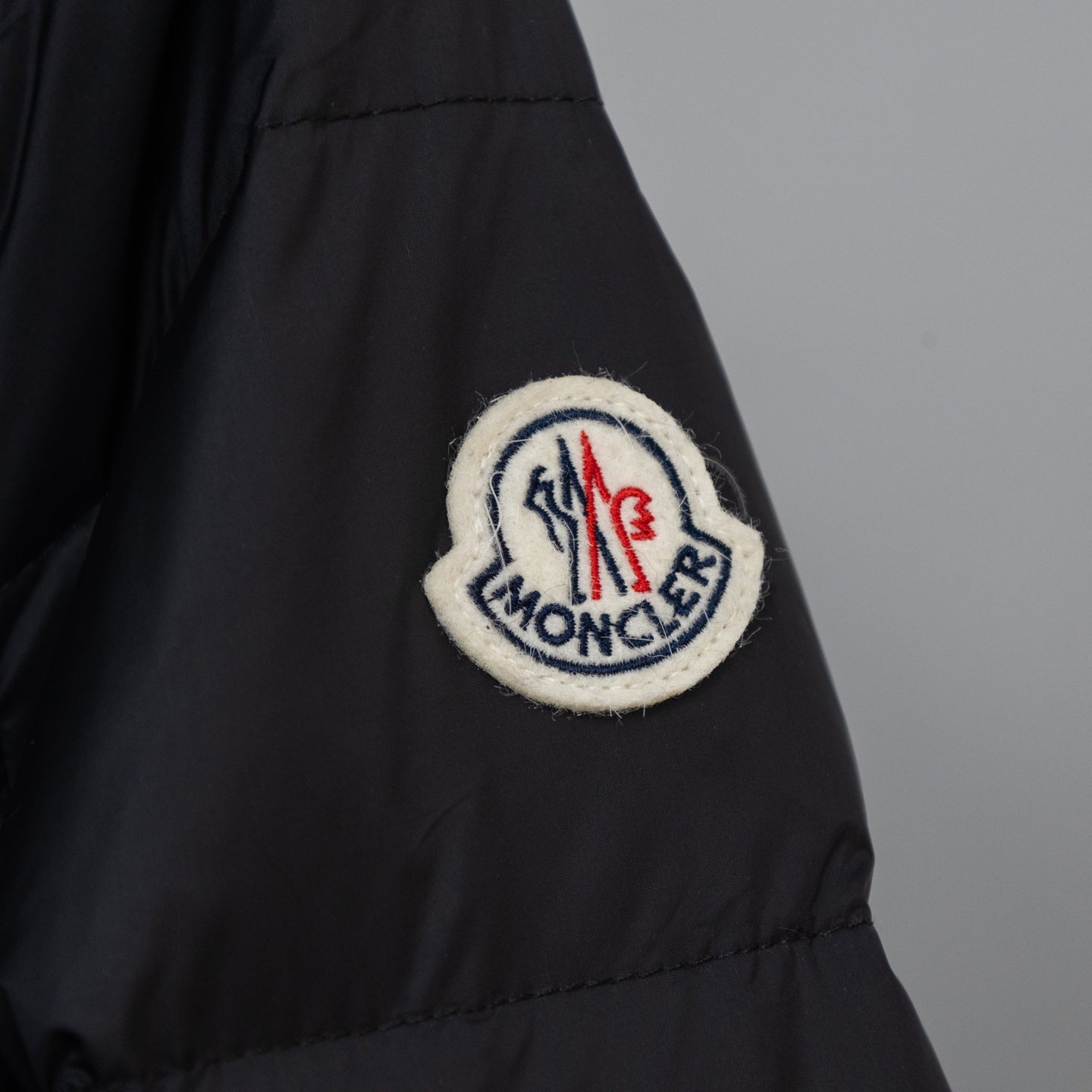 Moncler embroidered logo patch on long puffer coat sleeve, dark color