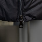 Long puffer jacket zipper detail with black pull tab on dark outer fabric.
