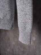 Light gray knit sweater sleeve and cuff detail, hanging on a hanger