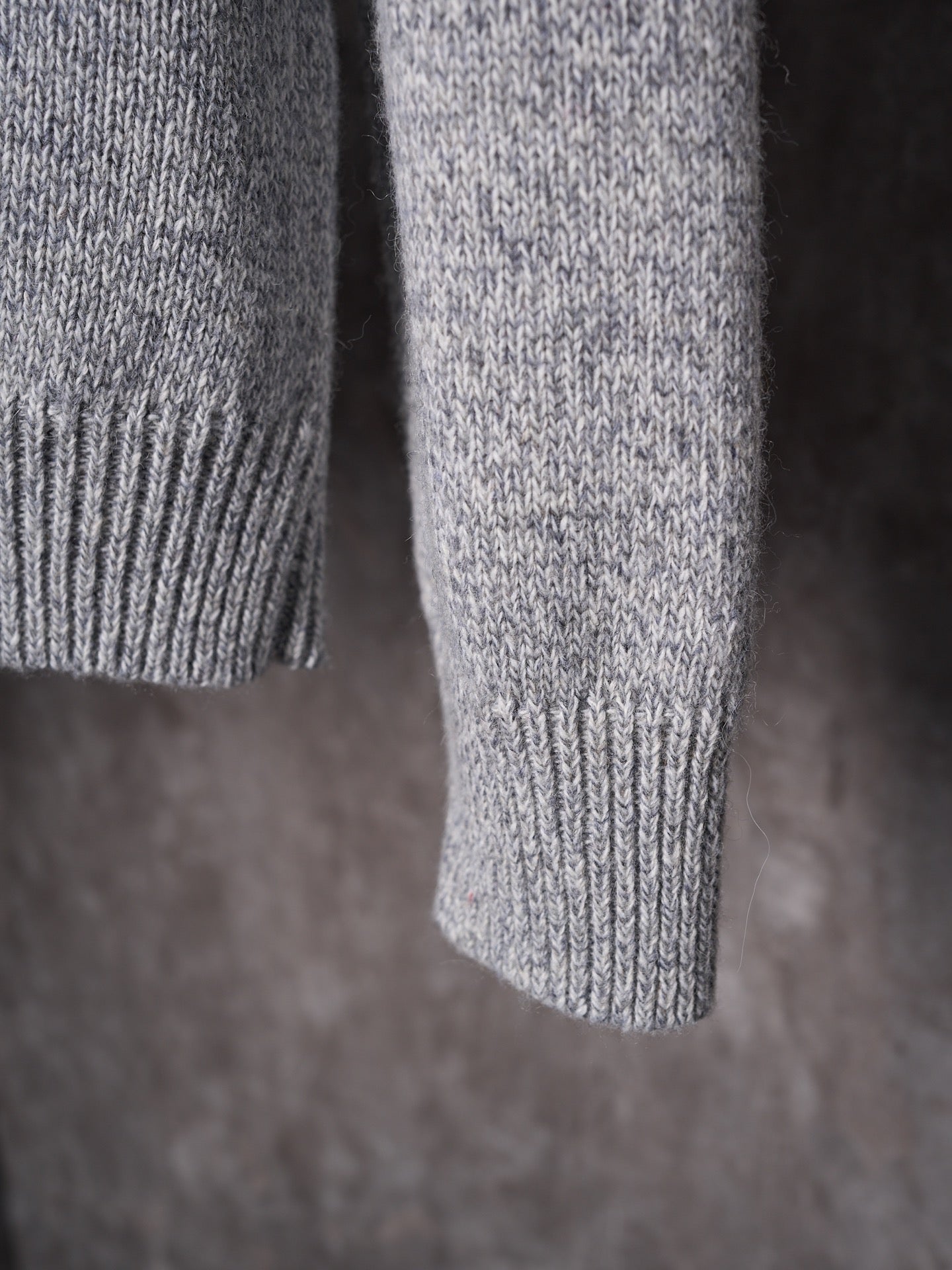 Light gray knit sweater sleeve and cuff detail, hanging on a hanger