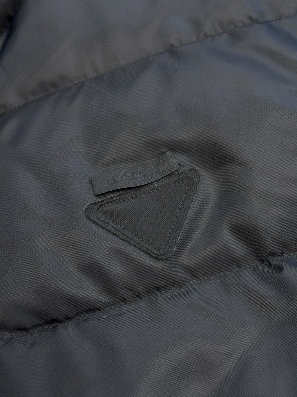 Prada dark puffer jacket close-up of embroidered triangle chest logo