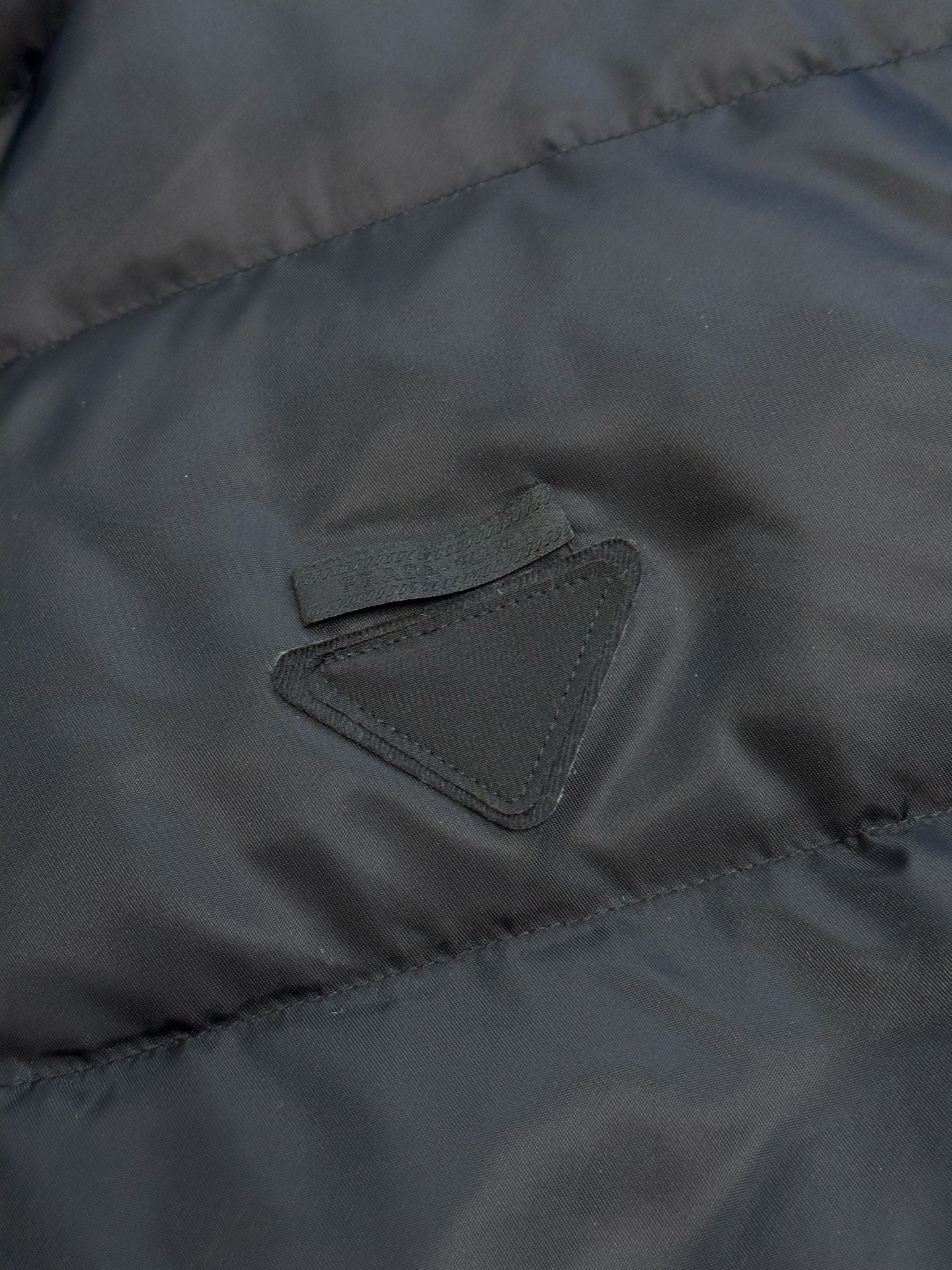 Prada dark puffer jacket close-up of embroidered triangle chest logo