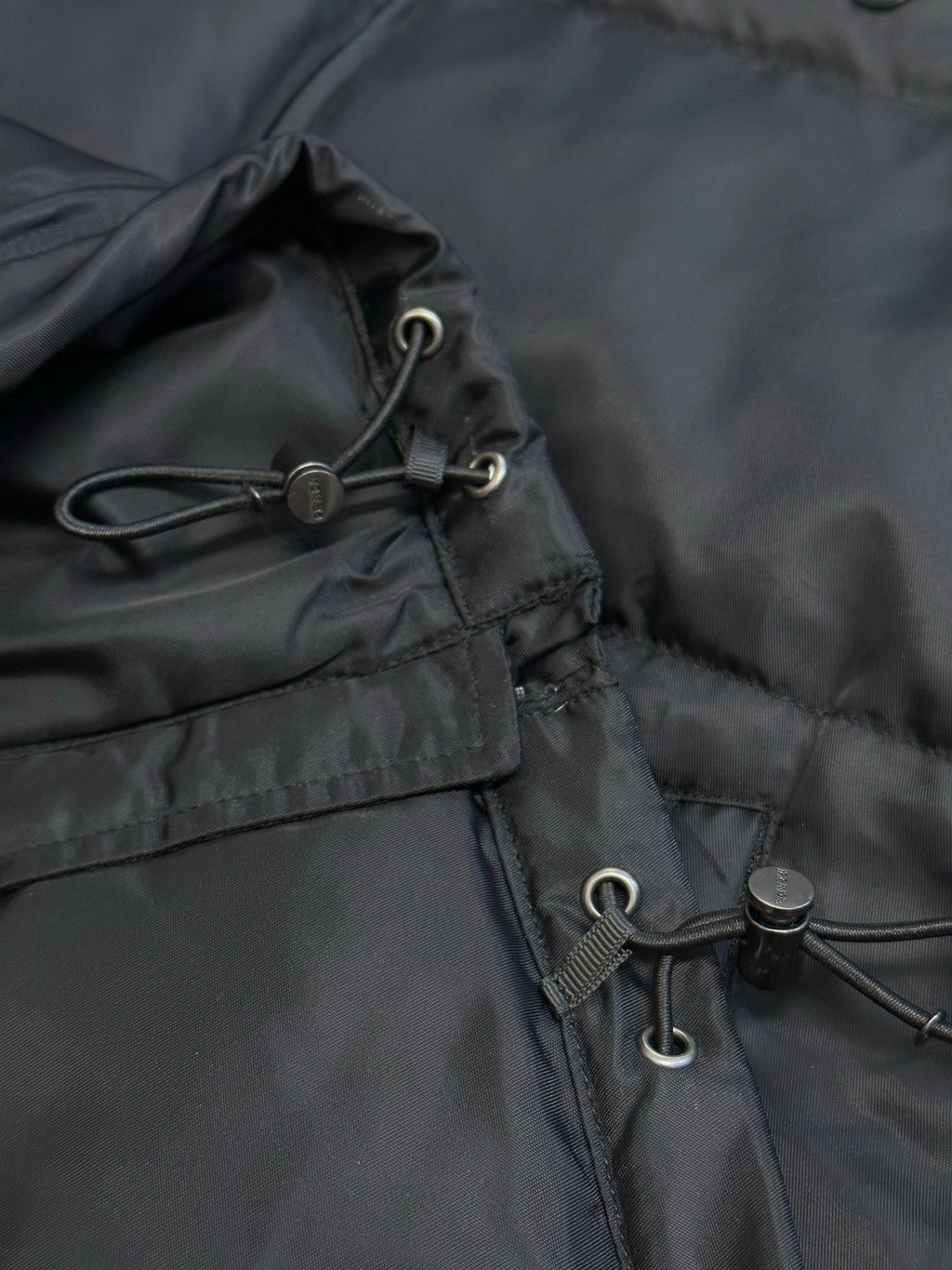 Prada dark puffer jacket close-up of hood drawstring with metal toggles