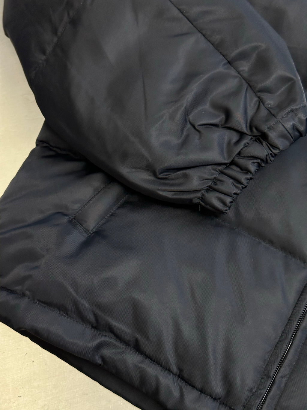 Prada dark puffer jacket close-up of sleeve cuff and quilted lower hem