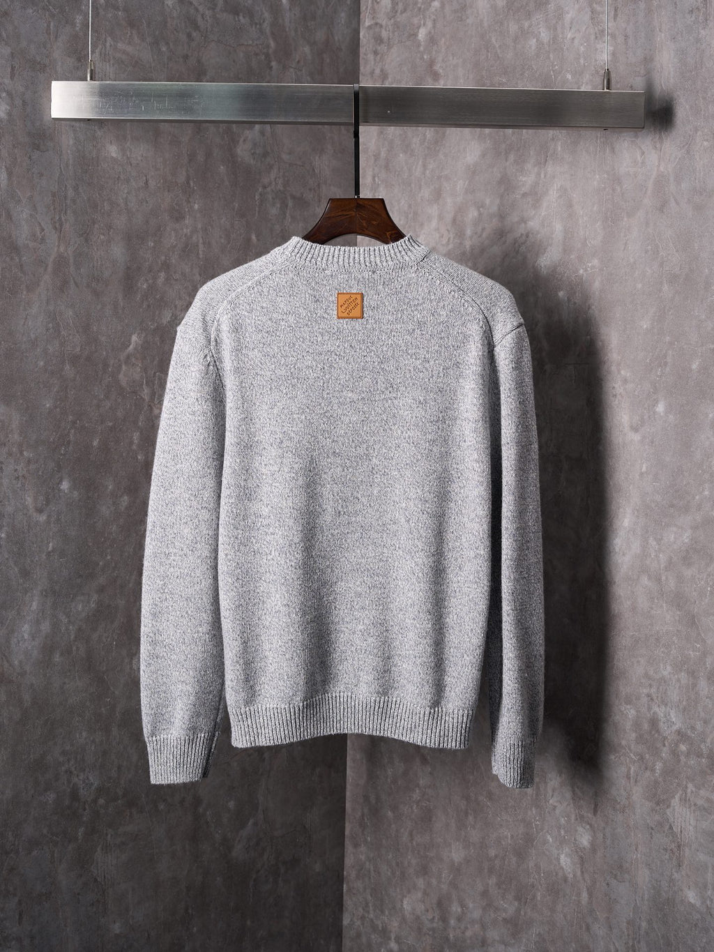 Light gray knit sweater with crew neck; small square chest logo patch
