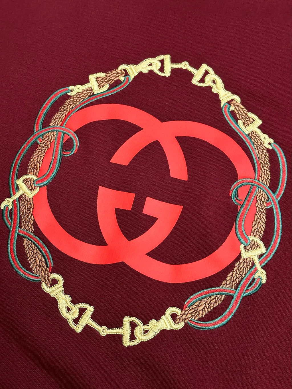 Maroon sweatshirt with oversized red GG logo framed by gold chain and teal trim