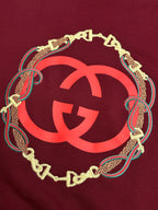 Maroon sweatshirt with oversized red GG logo framed by gold chain and teal trim