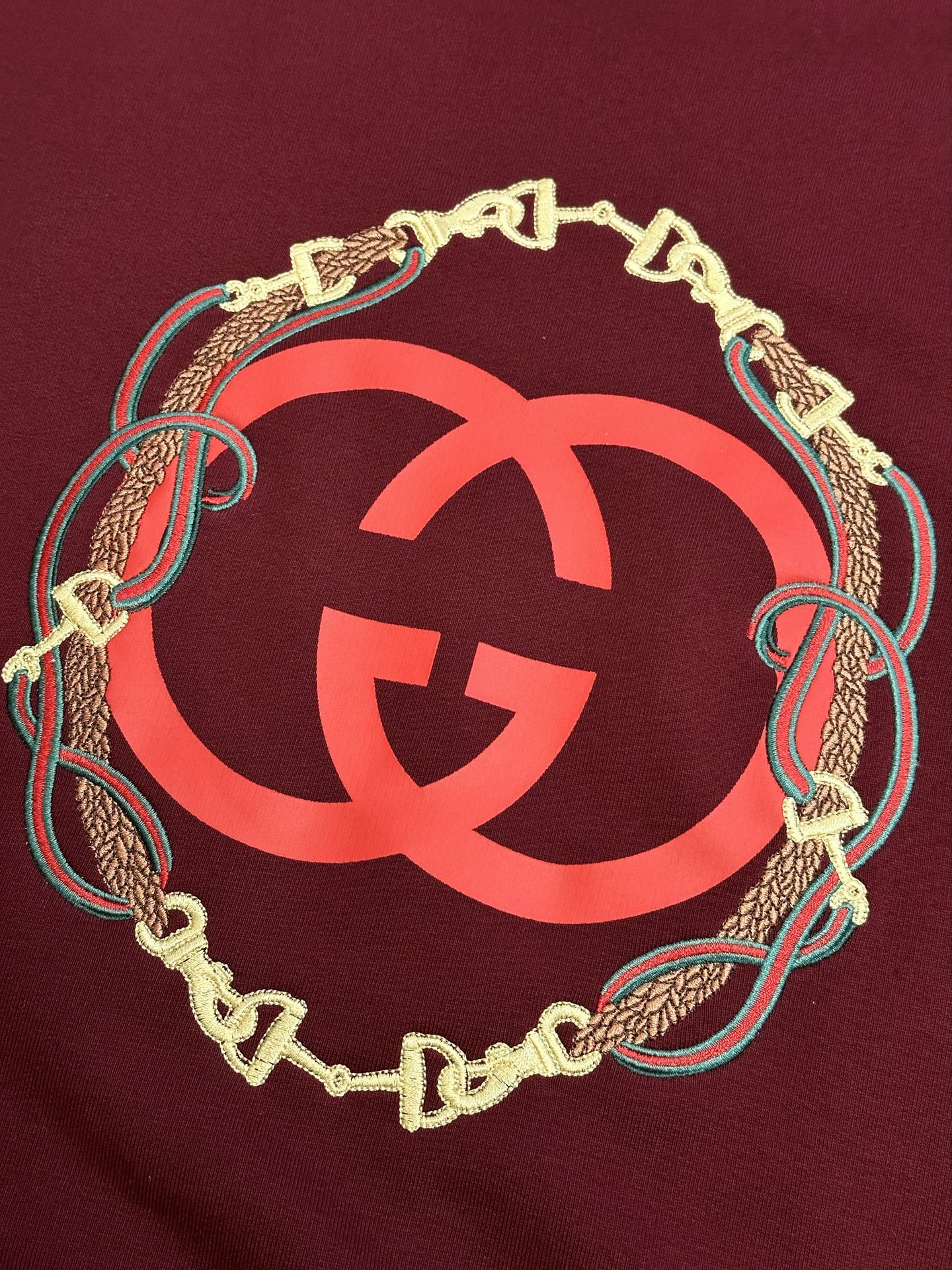 Maroon sweatshirt with oversized red GG logo framed by gold chain and teal trim