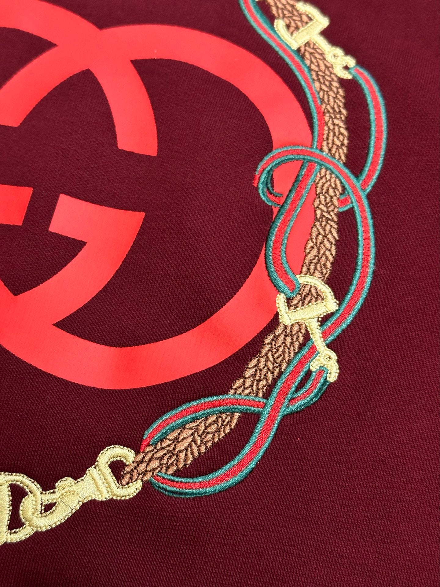 Maroon sweatshirt detail: red GG logo edge with gold chain and teal cord trim