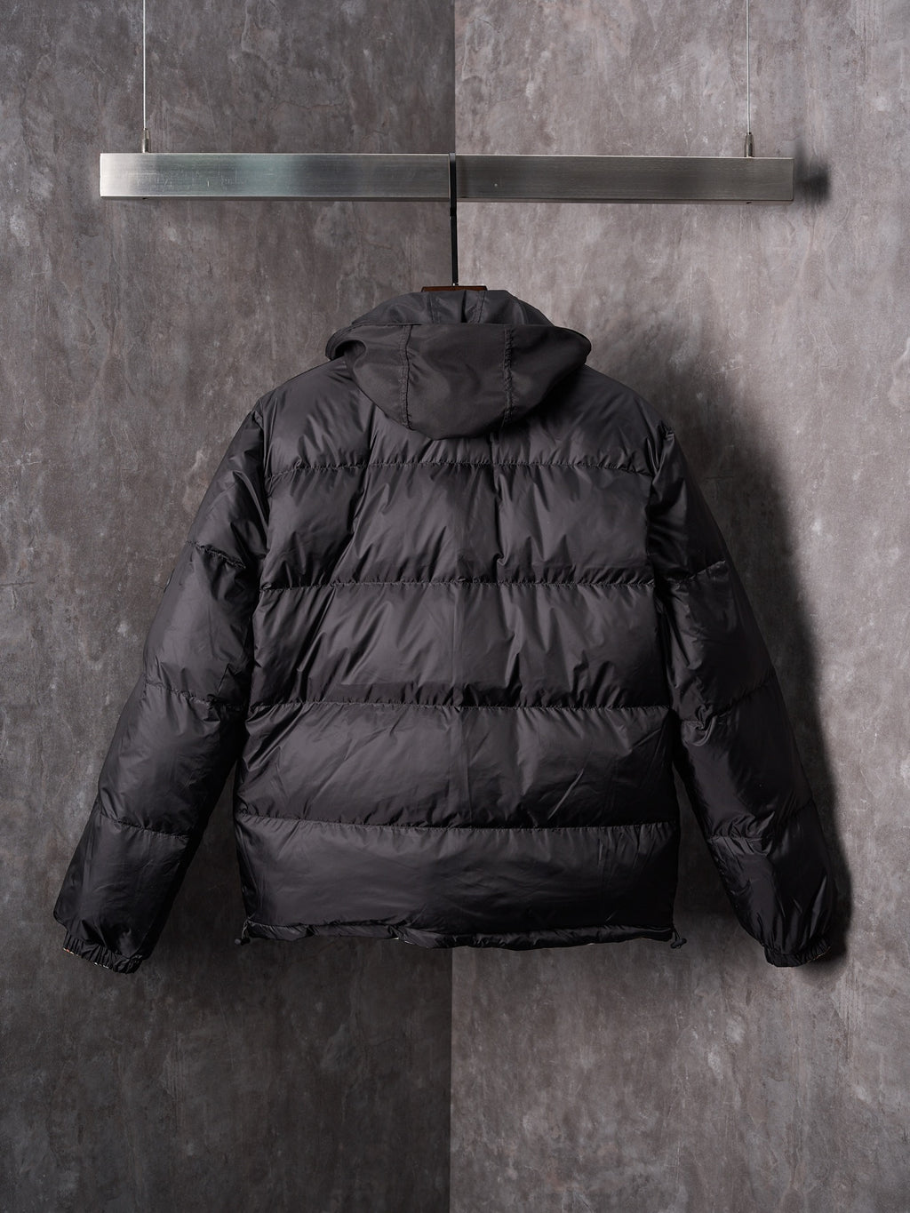 Black puffer jacket back view with attached hood and padded horizontal quilting.