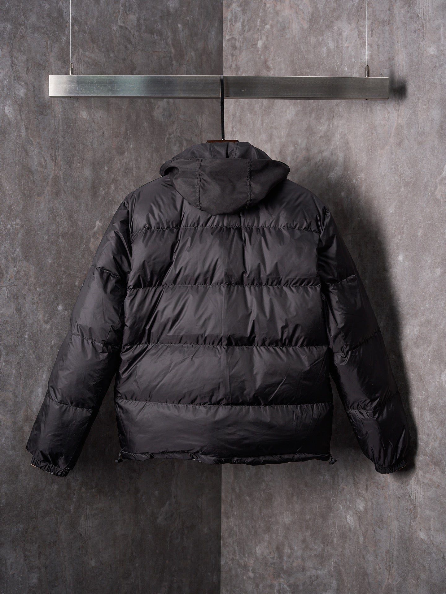 Black puffer jacket back view with attached hood and padded horizontal quilting.