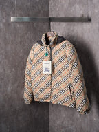 Plaid puffer jacket with black hood and front zip, featuring a hang tag at chest.