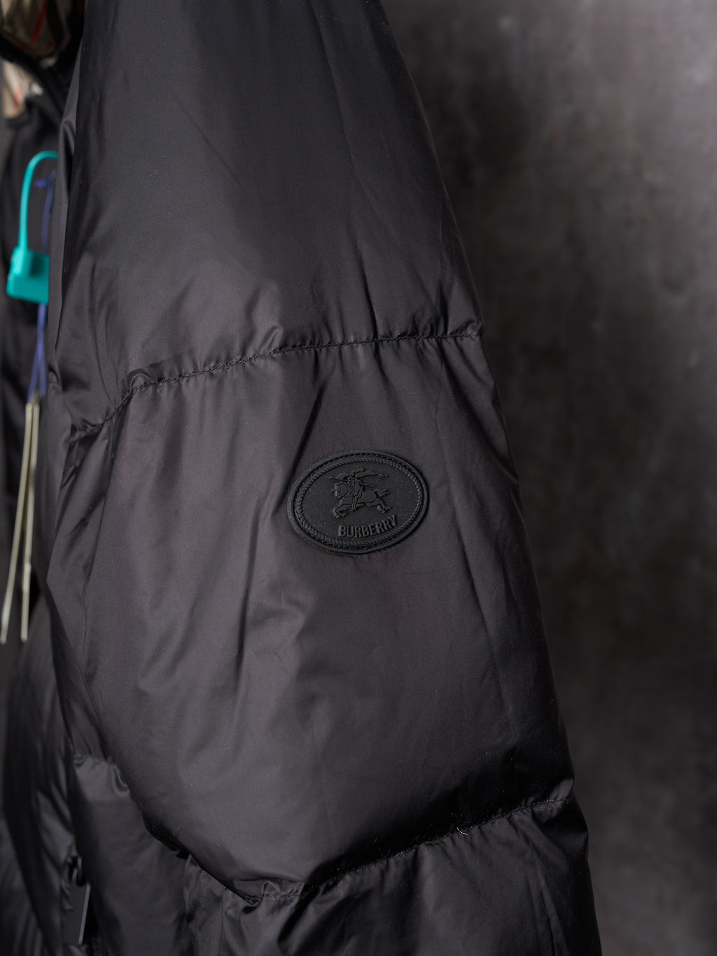Black puffer jacket close-up with circular logo patch on padded sleeve panel.