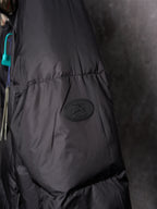 Black puffer jacket close-up with circular logo patch on padded sleeve panel.