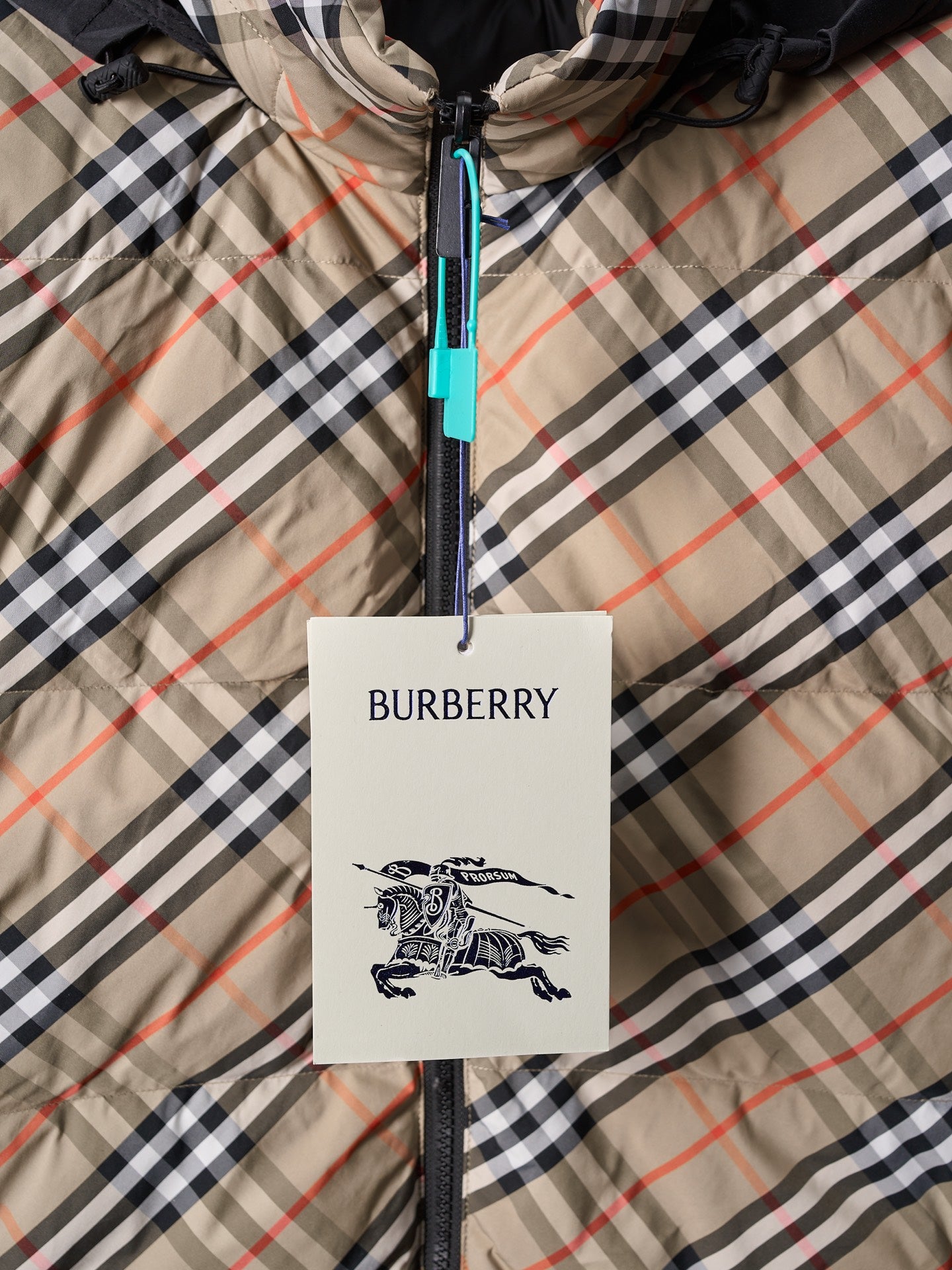 Plaid puffer jacket front close-up with zipper and Burberry hang tag at center.