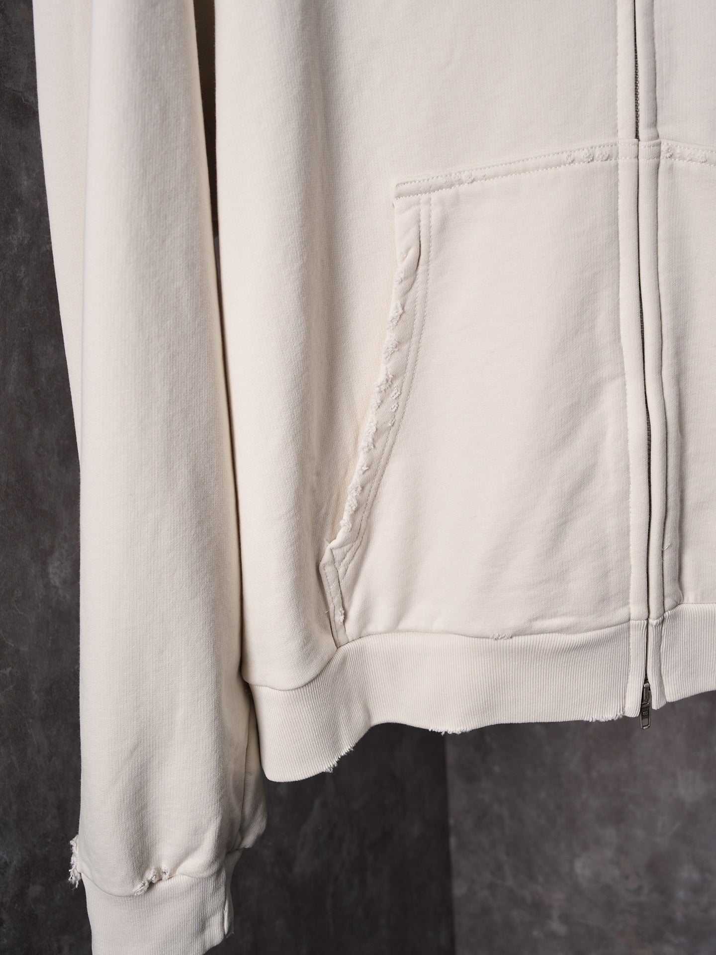 White long-sleeve hoodie with front pocket and ribbed cuffs, distressed hem