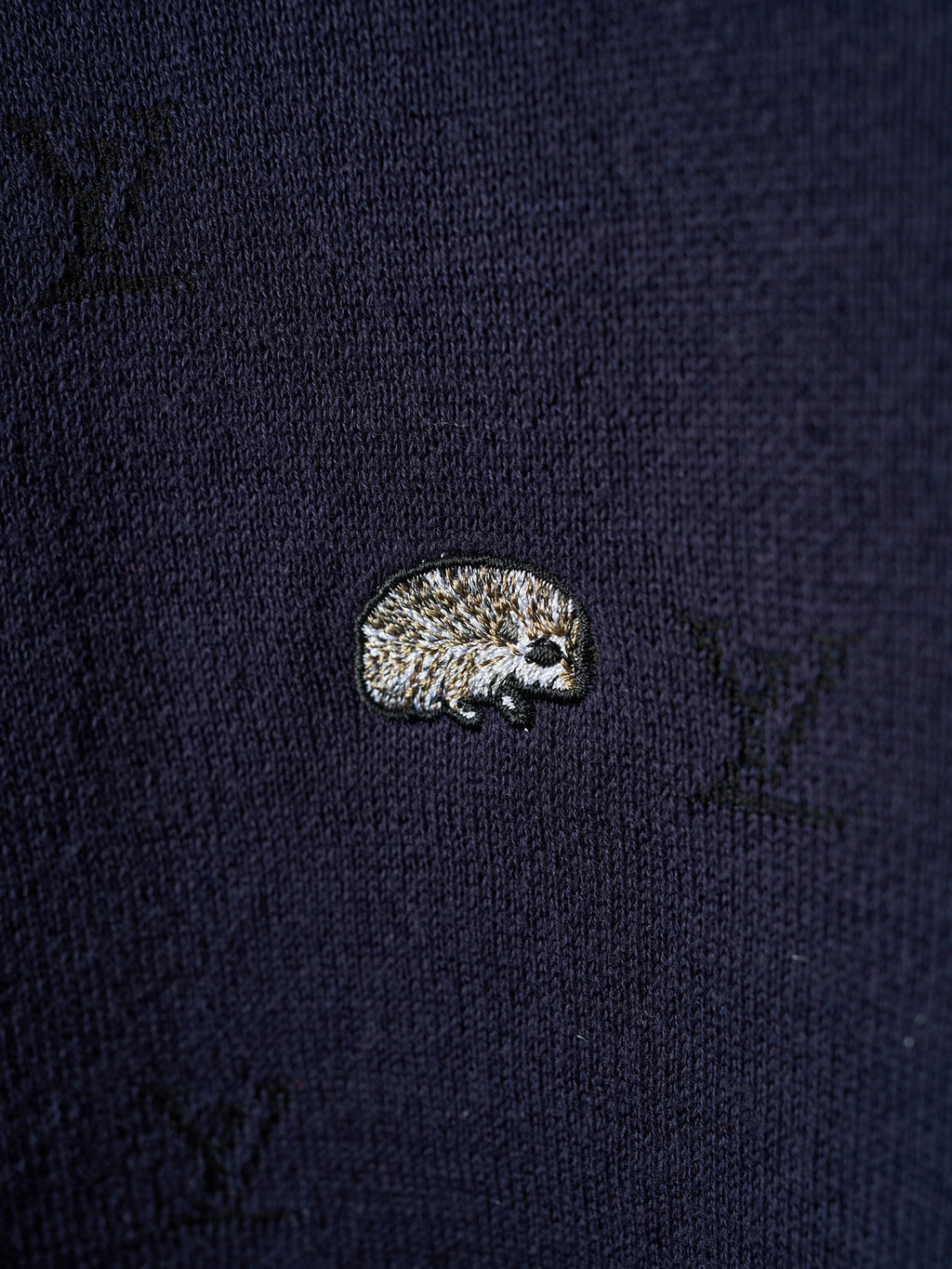 Close-up of dark navy knit sweater fabric with small textured animal emblem