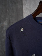 Close-up of dark navy knit sweater shoulder with small multicolor animal logo