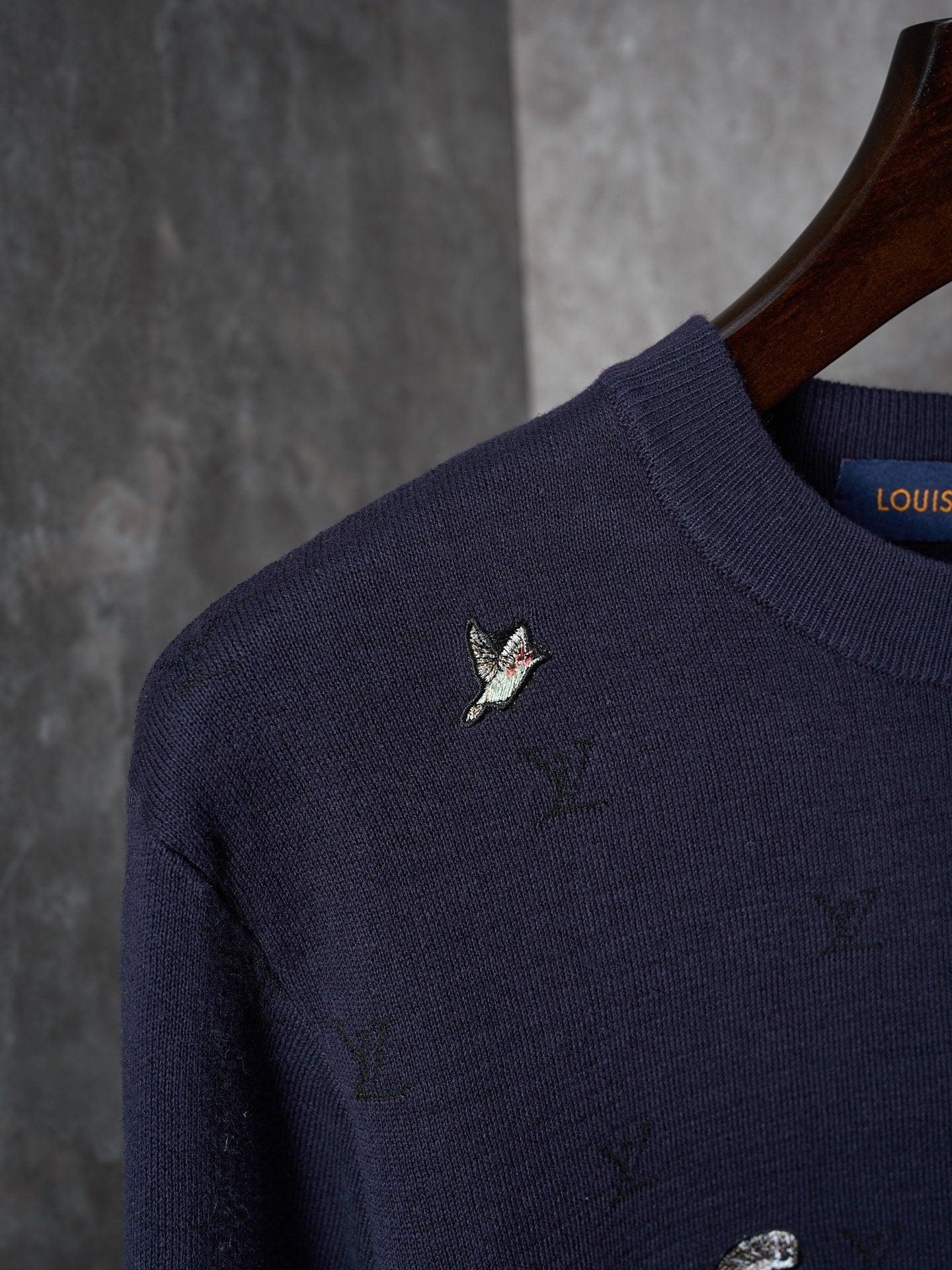 Close-up of dark navy knit sweater shoulder with small multicolor animal logo
