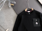 Black long-sleeve sweatshirt close-up with chest pocket and round logo patch