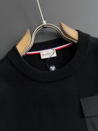 Black crewneck sweatshirt with ribbed collar and round logo patch at pocket