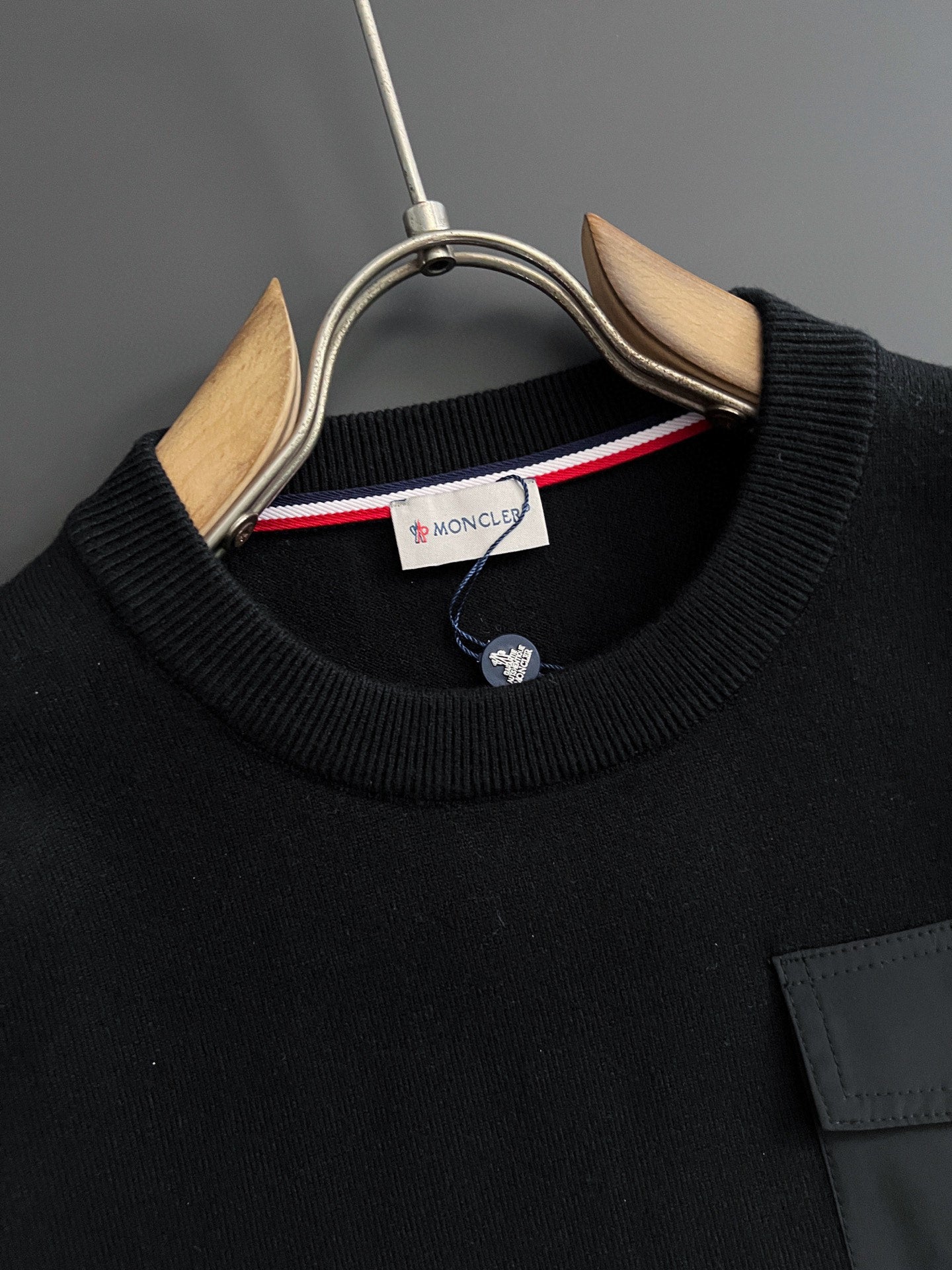 Black crewneck sweatshirt with ribbed collar and round logo patch at pocket