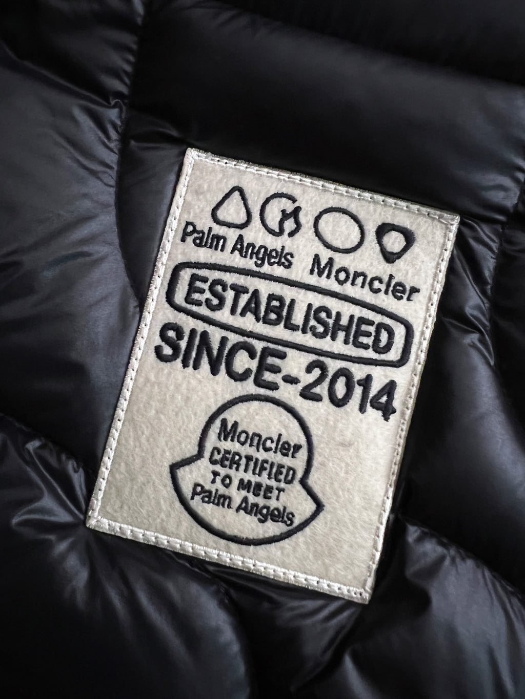 Moncler logo label patch on black puffer jacket with Palm Angels and Established text