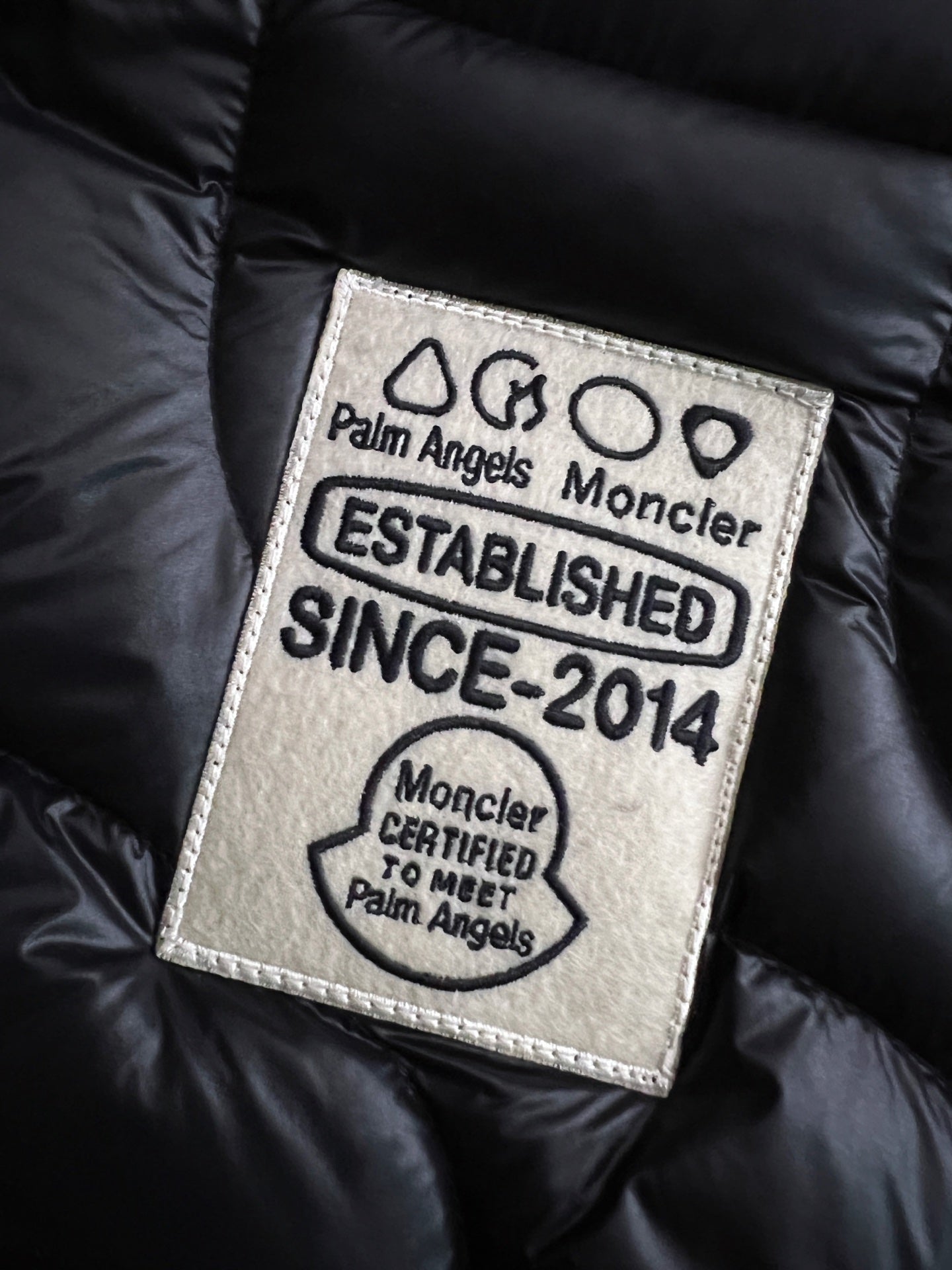 Moncler logo label patch on black puffer jacket with Palm Angels and Established text