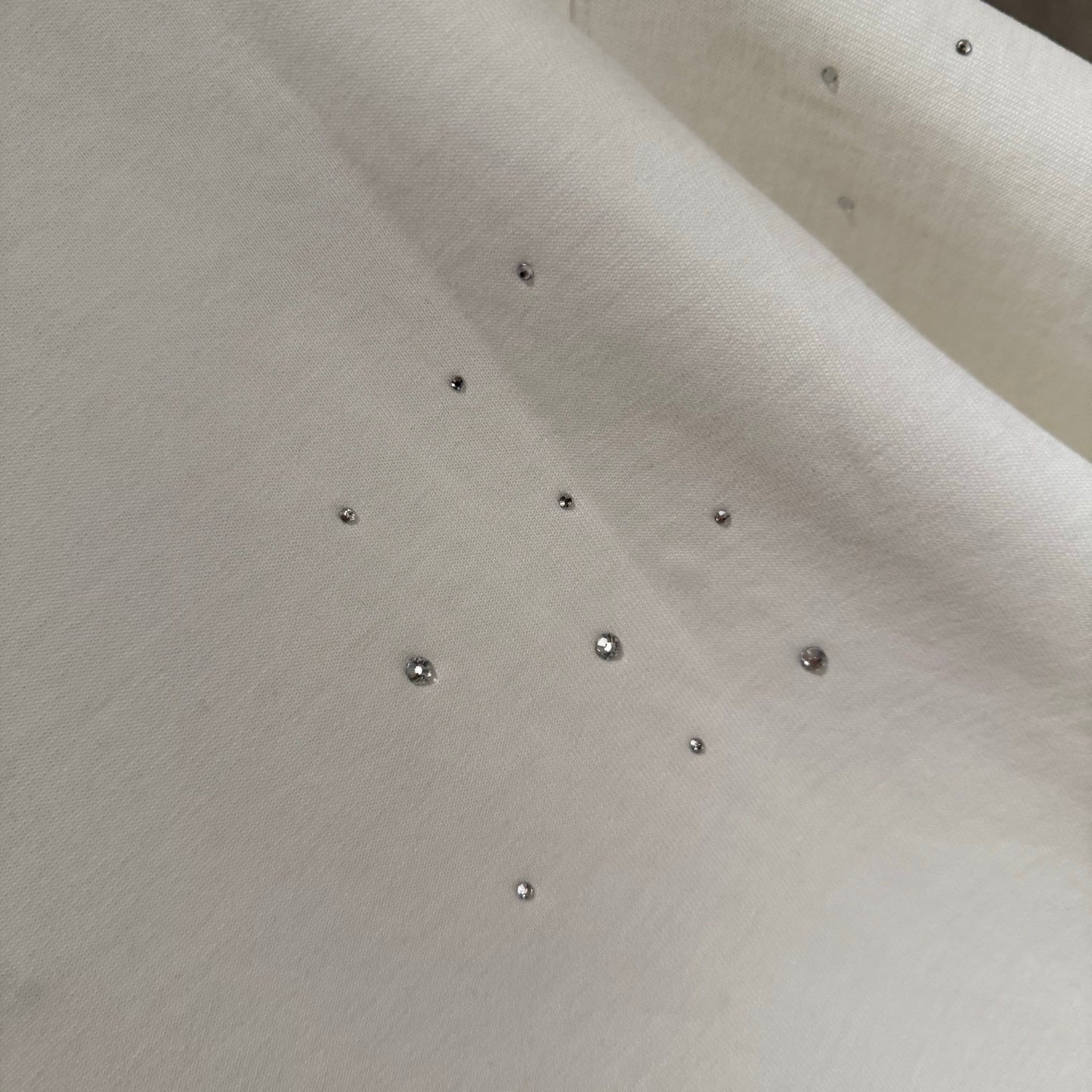White T-shirt fabric with scattered rhinestone studs across the surface