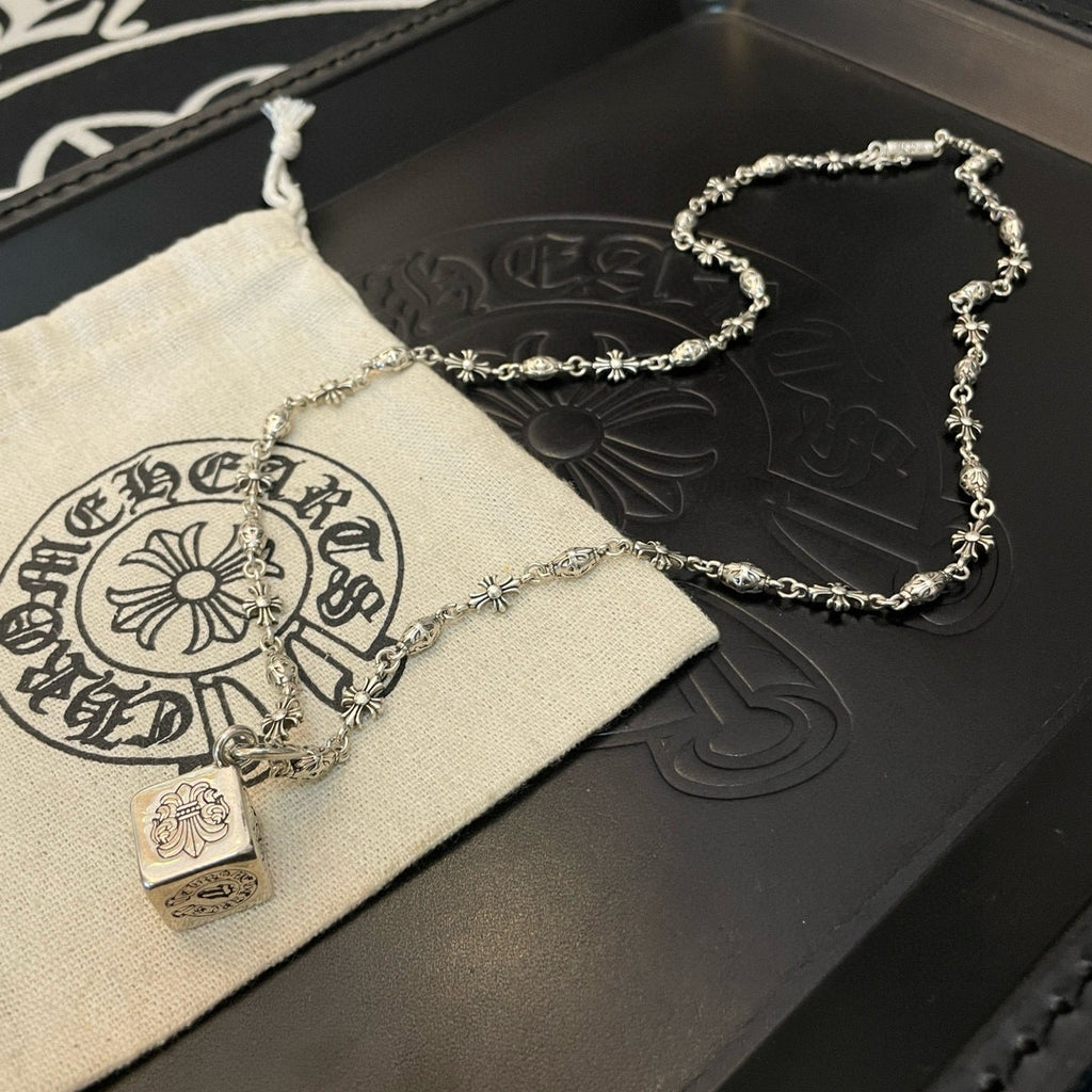 Silver chain necklace with square pendant on pouch beside dark leather case