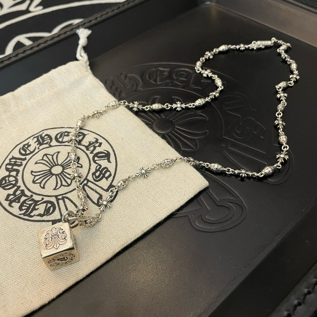 Silver chain necklace with square pendant on pouch beside dark leather case