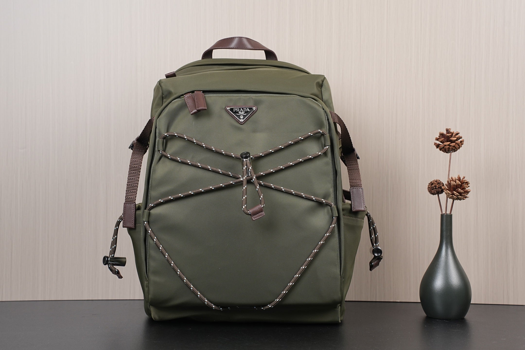Olive green Prada-style backpack with front zipper pocket and braided trim