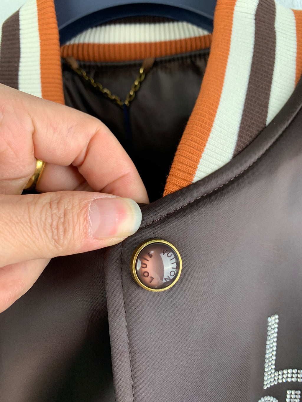 Louis Vuitton bomber jacket button, striped collar trim, gold-tone round snap detail close-up