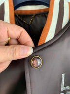 Louis Vuitton bomber jacket button, striped collar trim, gold-tone round snap detail close-up