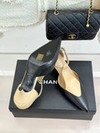 Beige and black pointed-toe slingback heels with ankle straps, on display box.