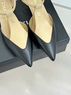 Close-up of beige pointed-toe slingback heels with ankle straps on black box.
