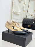 Beige and black pointed-toe slingback heels with ankle strap, on display box.