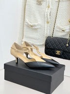 Beige and black pointed-toe slingback heels with ankle strap, on display box.