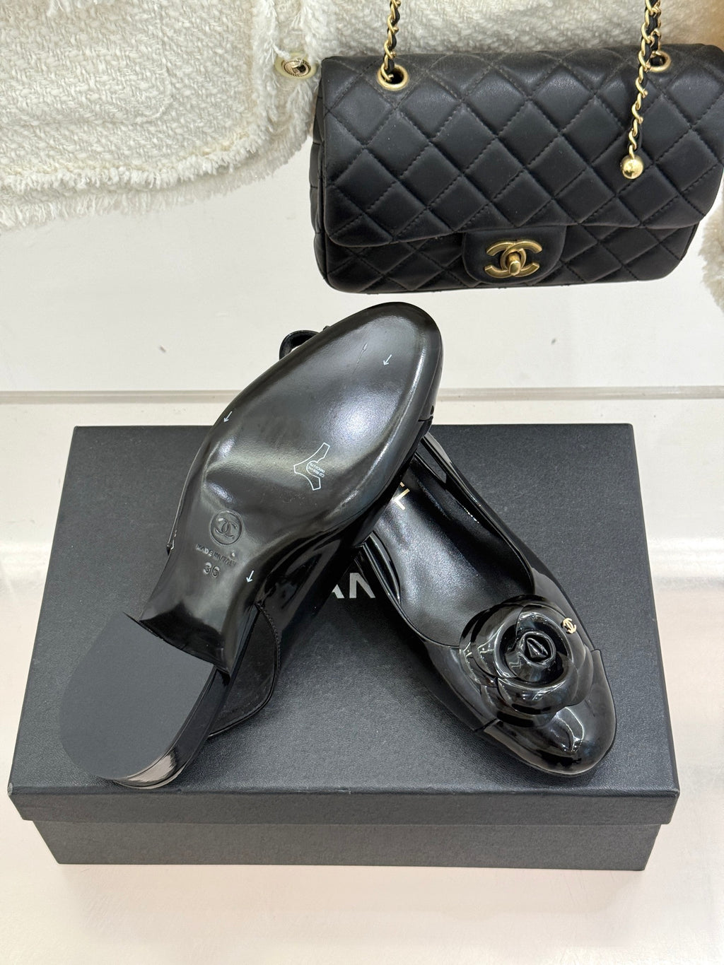 Black patent leather slingback flats with gold CC medallion on a dark shoe box