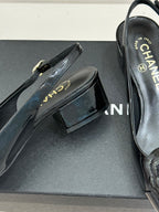Black patent leather flat shoe with gold-tone buckle strap on a dark shoe box