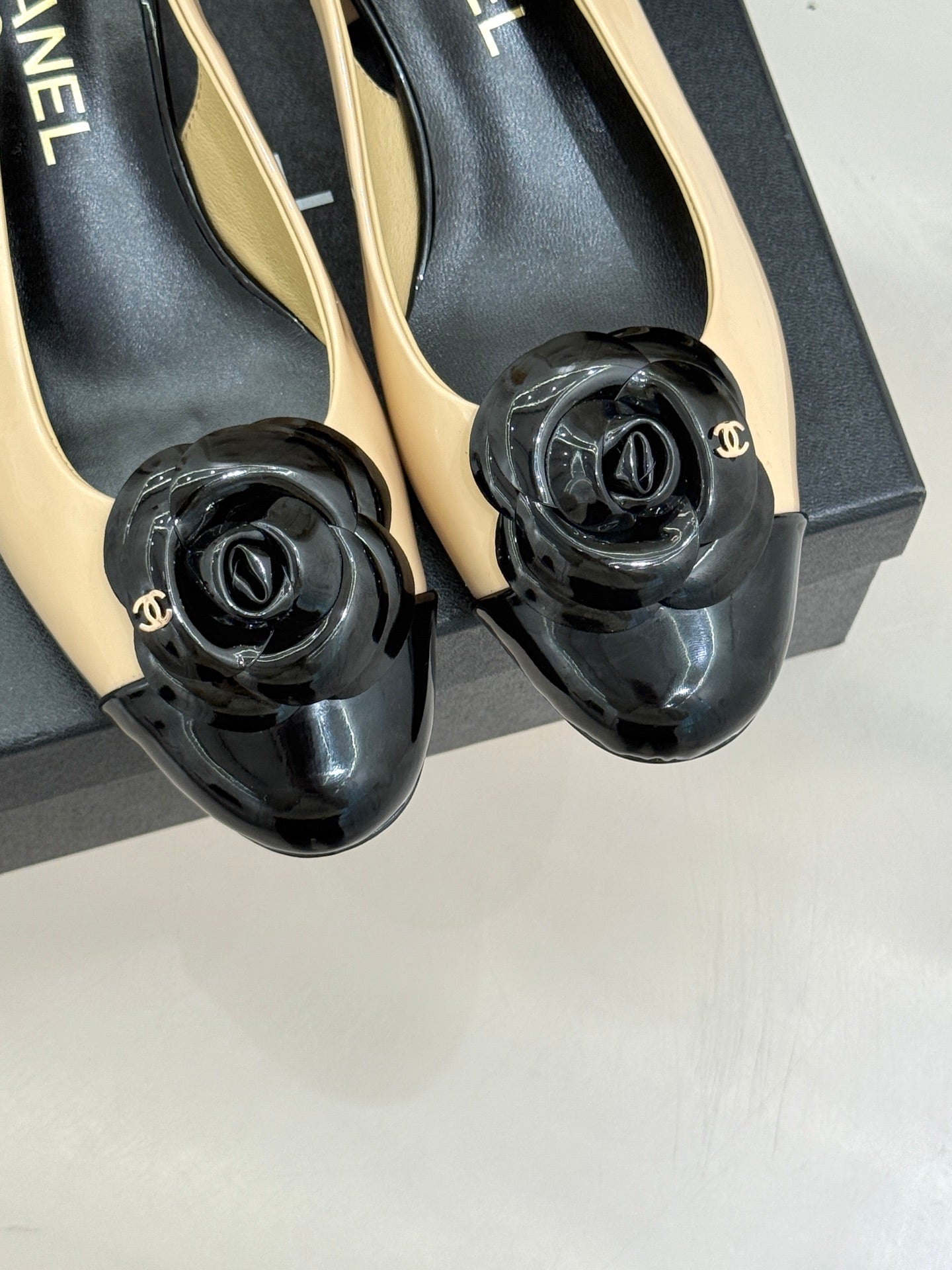 Women’s Chanel slingback heels close-up, black glossy rosette on cream strap