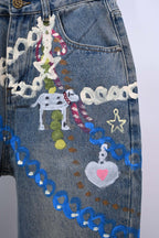 Denim pants with multicolor charm patchwork and blue chain trim across the leg