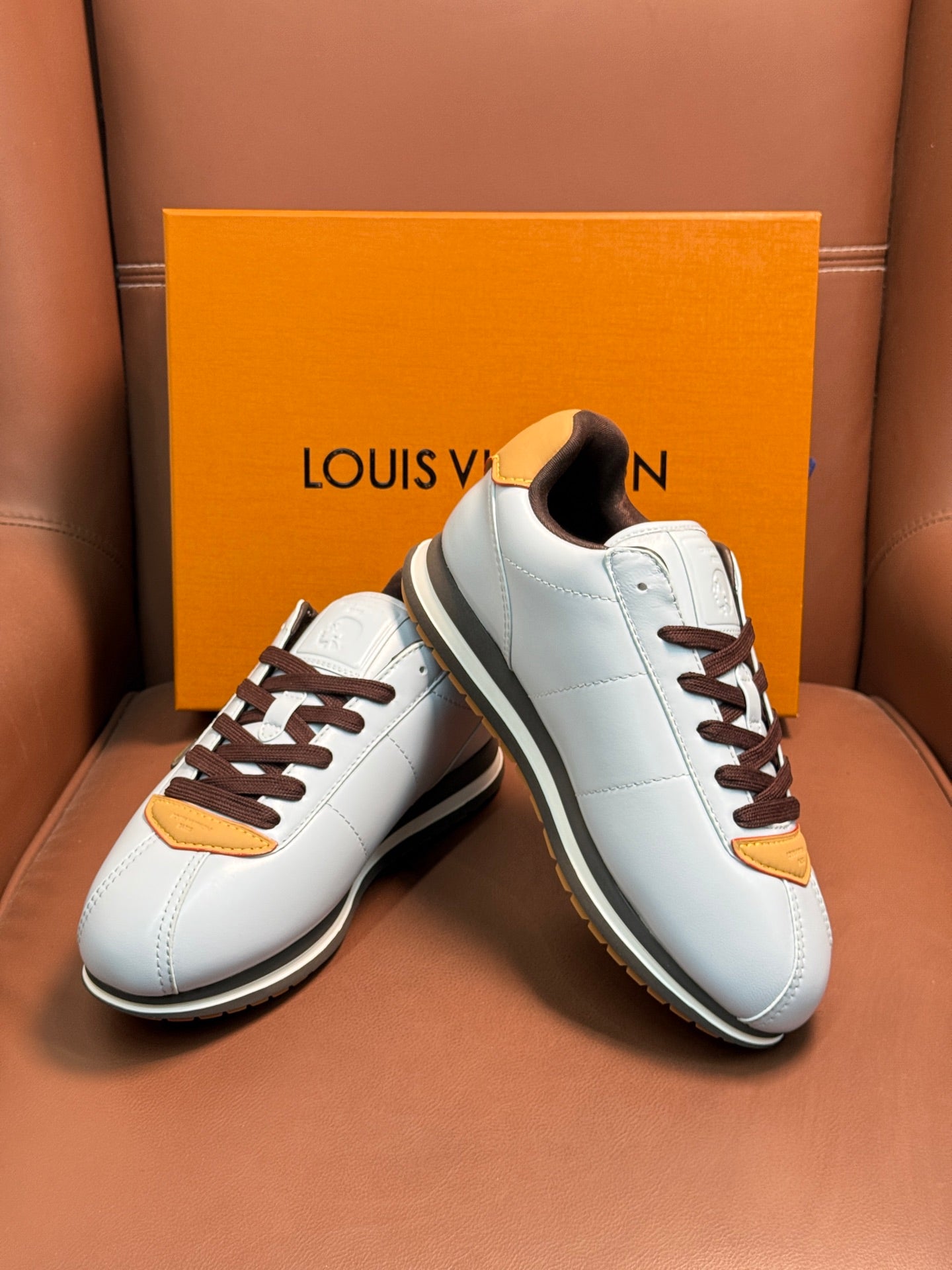 White Louis Vuitton low-top sneakers with brown laces, yellow heel trims, and dark lining