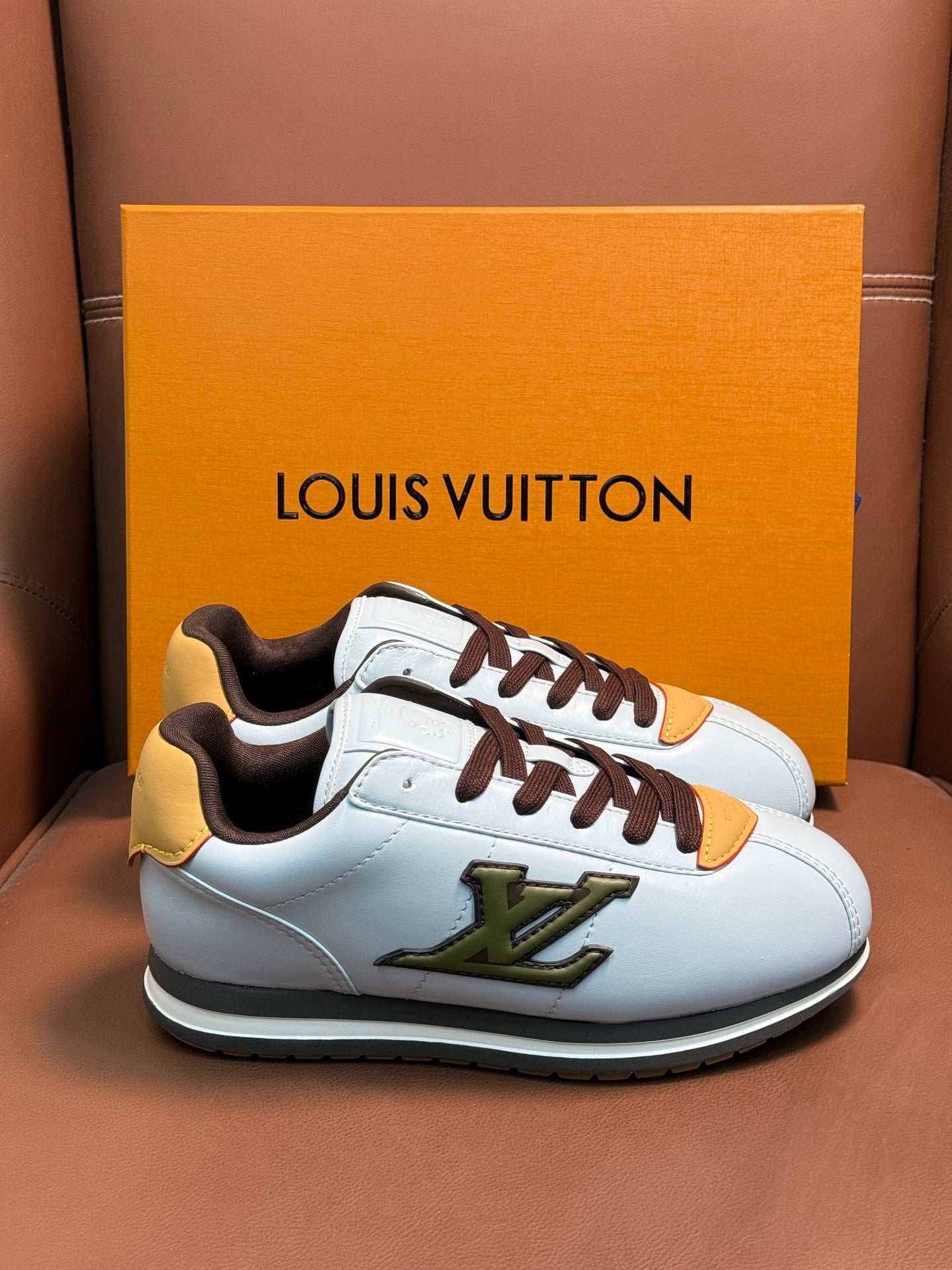 White Louis Vuitton low-top sneakers with brown laces, yellow heel patch, and green logo