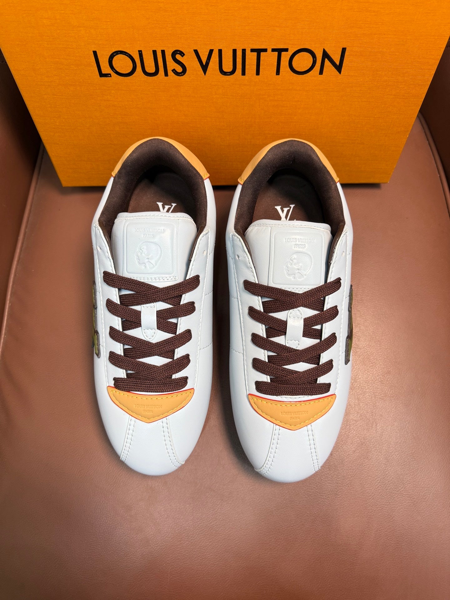 Pair of white Louis Vuitton low-top sneakers with brown laces and yellow curved accents