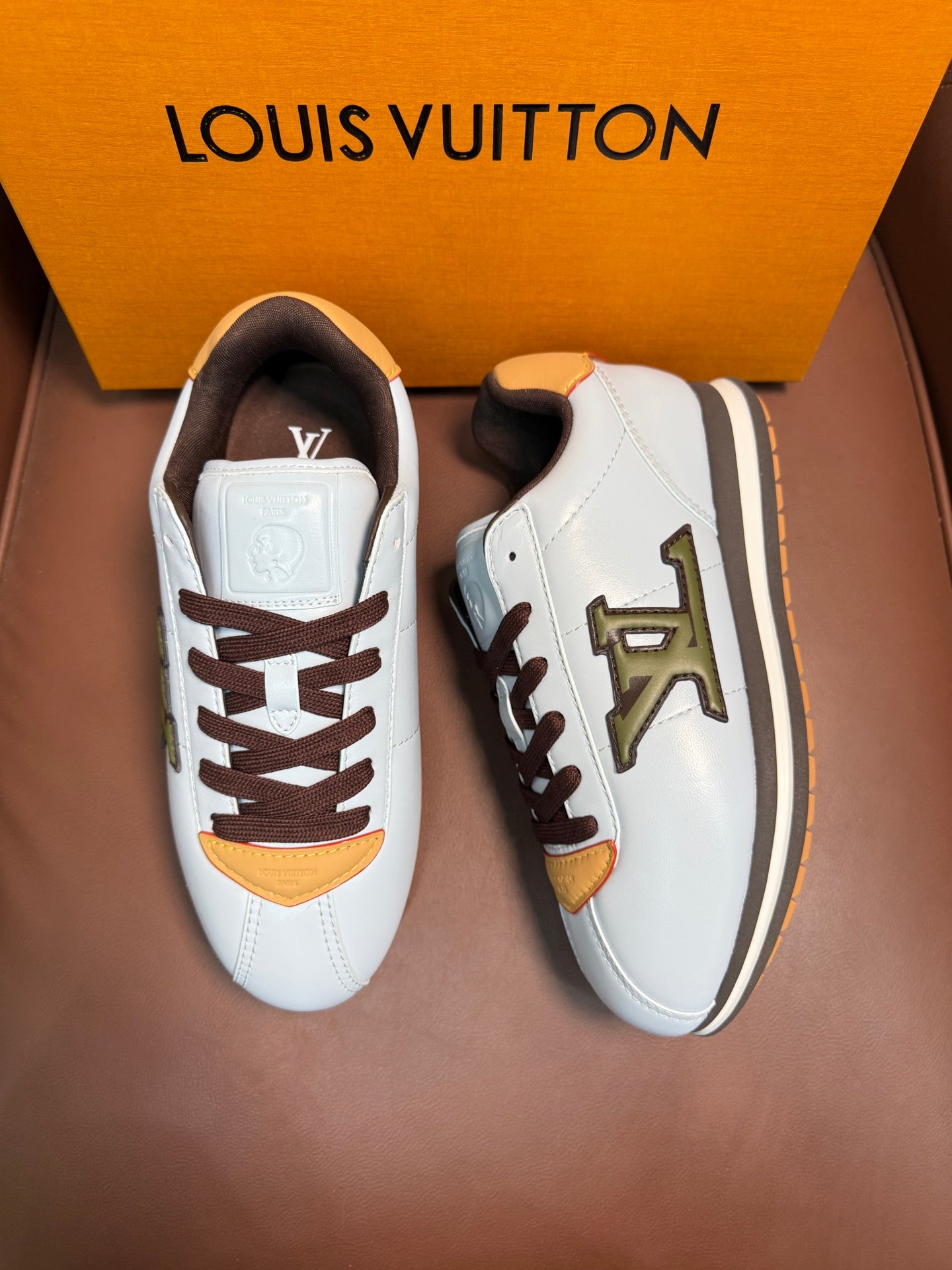 Pair of white Louis Vuitton sneakers with brown laces, yellow trims, and side LV emblem