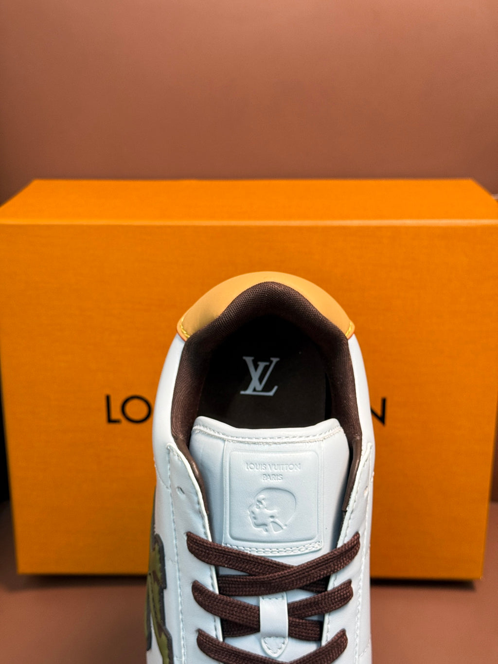 White Louis Vuitton sneaker toe view with brown laces, yellow side trim, and black tongue logo