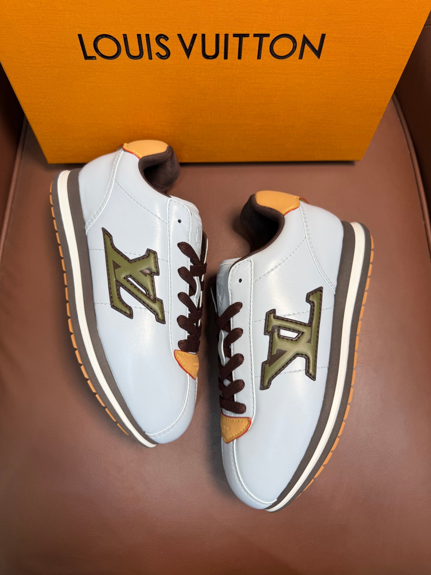Pair of white Louis Vuitton low-top sneakers with brown laces, yellow trims, and green logo
