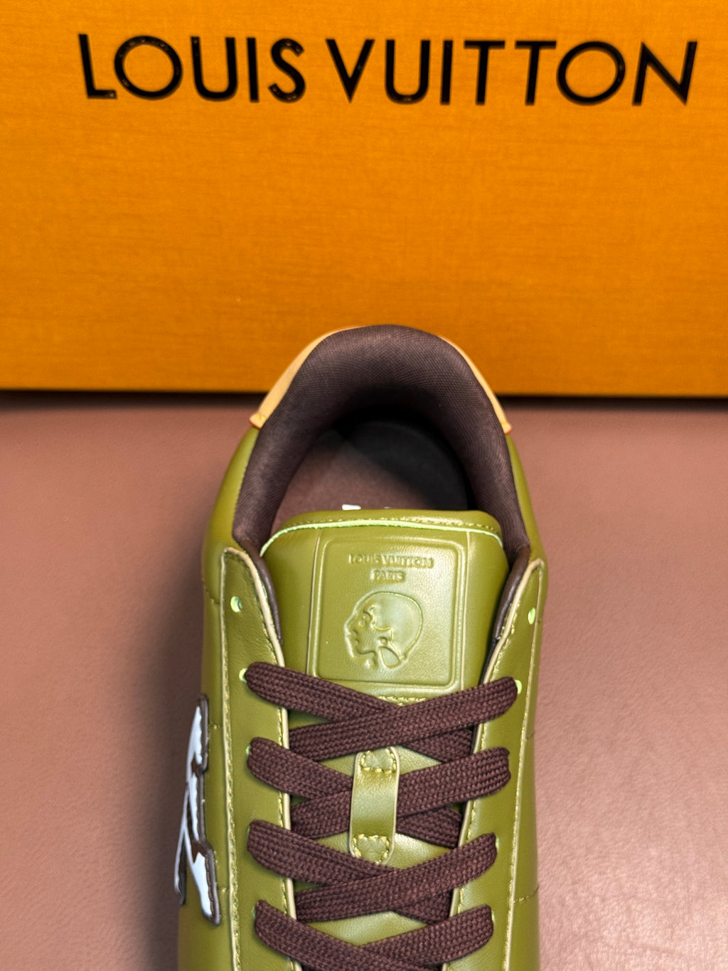 Green sneaker close-up with dark brown laces and embossed logo on tongue