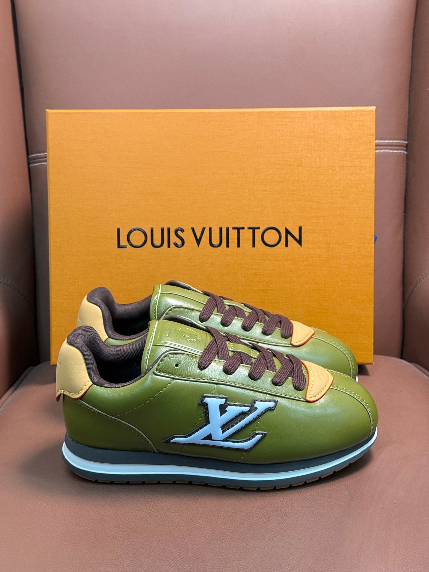 Green leather sneakers with dark brown laces, orange heel accents, and LV logo